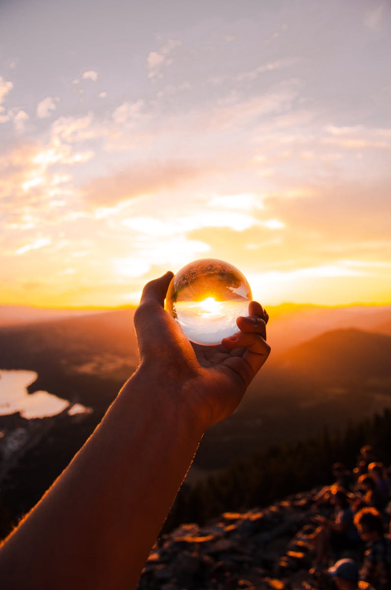 Captivating sunset view reflected in a crystal ball held by hand, overlooking a scenic landscape.